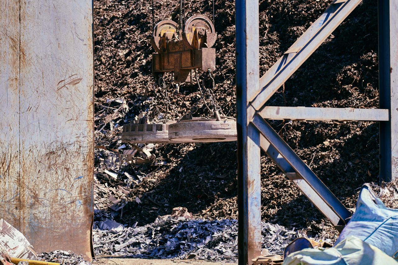 our-story-01 Magnetic crane sorting metal in an industrial scrapyard. Bright daylight highlights the steel and machinery.