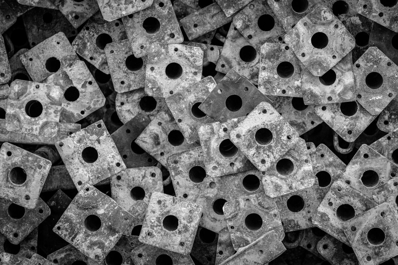 services-05 A close-up abstract composition of stacked, perforated metal plates in black and white, showcasing texture and pattern.